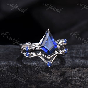 May include: A silver ring set featuring a kite-shaped, deep blue gemstone as the focal point. The ring is accented with smaller blue gemstones and a branch-like design. The set includes a matching band, creating a cohesive and elegant look.