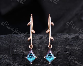 May include: A pair of rose gold earrings with a delicate branch design and a square blue gemstone dangling from each earring.