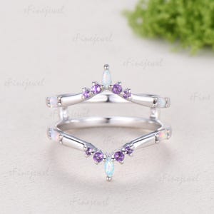 May include: A silver-toned ring guard featuring a chevron design with marquise-cut opals at the center points and round-cut purple amethyst stones along the bands. The metal band has a polished finish and includes small opals at the outer ends.