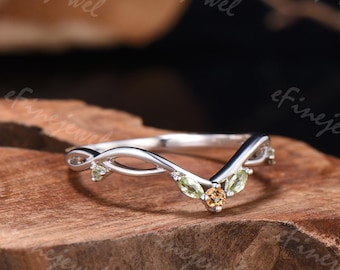 May include: A silver ring with a curved design, featuring small, light green and yellow gemstones. The ring has a delicate, nature-inspired aesthetic, with a V-shaped band and decorative accents.