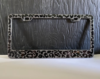 May include: Black license plate frame with a silver glitter leopard print design.
