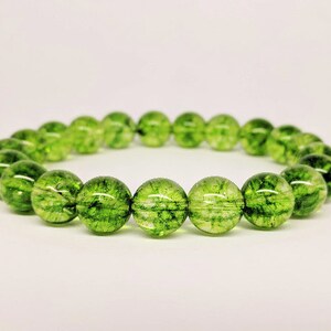 May include: A circular bracelet composed of numerous translucent, spherical green beads. Each bead features internal dark green inclusions and a crackled texture, creating a vibrant, moss-like appearance throughout the polished, reflective surface of the stones.