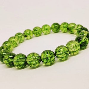 May include: A stretch bracelet composed of round, translucent green beads. Each bead features a distinct internal network of dark green, moss-like inclusions that create a unique, organic pattern throughout the polished, spherical surface of the stones.