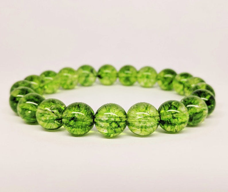 May include: A circular bracelet composed of numerous translucent, spherical green beads. Each bead features internal dark green inclusions and a crackled texture, creating a vibrant, moss-like appearance throughout the polished, reflective surface of the stones.