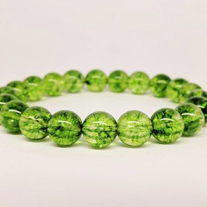 May include: A circular bracelet composed of numerous translucent, spherical green beads. Each bead features internal dark green inclusions and a crackled texture, creating a vibrant, moss-like appearance throughout the polished, reflective surface of the stones.