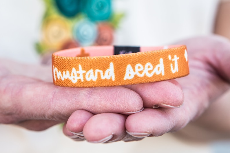 May include: A mustard yellow wristband with the text "mustard seed it" in white lettering.