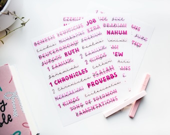May include: A set of pink and white Bible book labels with the names of the books of the Bible printed in black. The labels are on a white background.