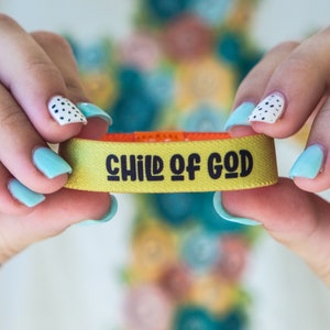 May include: A yellow wristband with the text "CHILD OF GOD" in black lettering.