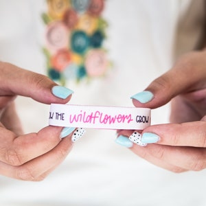May include: White wristband with the text "Let the wildflowers grow" in pink lettering.
