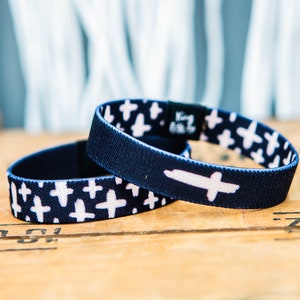 May include: Two blue elastic bracelets with a white cross pattern. One bracelet has a larger white cross on it.