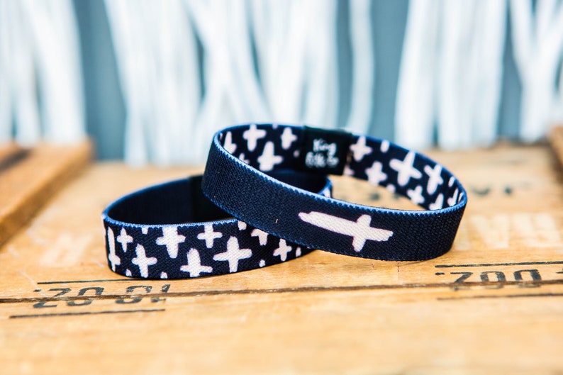 May include: Two blue elastic bracelets with a white cross pattern. One bracelet has a larger white cross on it.