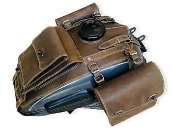 May include: Brown leather motorcycle tank bag with two side bags. The tank bag has a large flap with buckles and a small pocket on the front. The side bags have a single buckle closure.