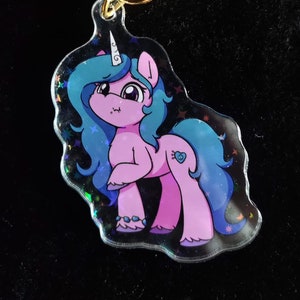 May include: A pink and blue unicorn keychain with a gold star-shaped clasp. The unicorn has a heart-shaped marking and a blue mane and tail. The keychain is made of clear acrylic with a holographic effect.
