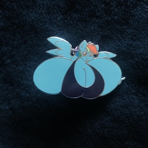 May include: A light blue enamel pin featuring a cartoon pony with a rainbow mane and tail. The pony is wearing a dark blue swimsuit. The pin has a silver border and is set against a dark blue background.