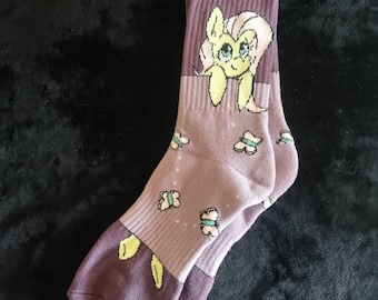 May include: Purple and light purple socks with a cartoon image of a yellow pony with pink hair and blue eyes. The socks have a pattern of green butterflies.