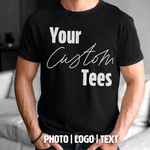 May include: Black t-shirt with the text "Your Custom Tees" in white. The shirt also has the text "PHOTO | LOGO | TEXT" at the bottom. The shirt is short-sleeved and appears to be made of a soft material.