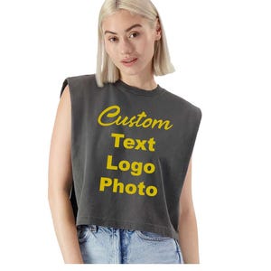 May include: A charcoal gray sleeveless crop top with the words "Custom Text Logo Photo" in yellow script. The top is paired with blue denim jeans. The model is wearing the top.