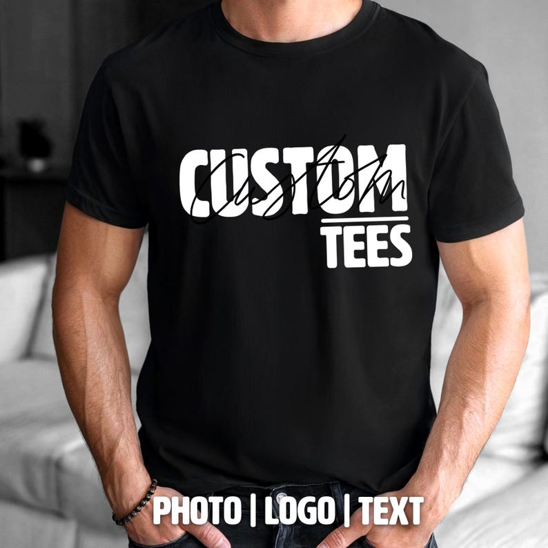 May include: Black t-shirt with the white text "CUSTOM TEES". The shirt has short sleeves and is being worn by a person. The bottom of the image has the text "PHOTO | LOGO | TEXT".