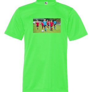 May include: A bright green t-shirt with a picture of a group of children playing soccer on the front. The children are wearing blue and red jerseys and are running with a soccer ball.