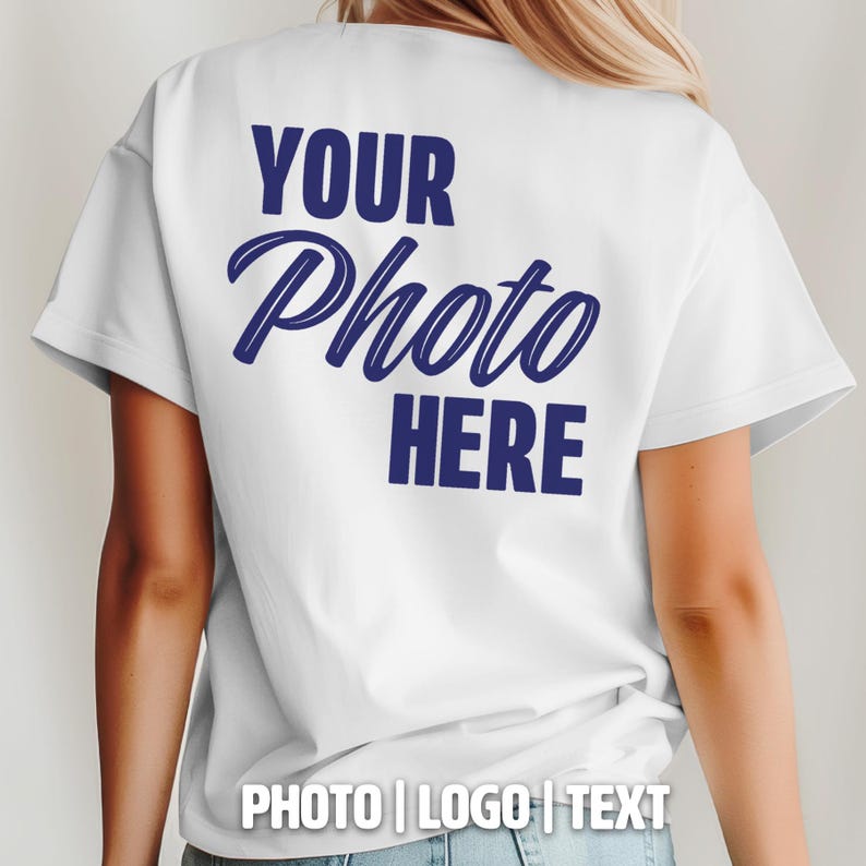 May include: White t-shirt with the text "YOUR Photo HERE" in navy blue script on the back. The bottom of the shirt has the text "PHOTO | LOGO | TEXT". The shirt is a basic crew neck.
