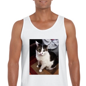 Peut inclure: Un d&eacute;bardeur blanc sans manches avec une impression graphique rectangulaire centr&eacute;e repr&eacute;sentant un chat noir et blanc aux marques tigr&eacute;es sur la t&ecirc;te, au nez rose et aux pattes blanches, assis avec les oreilles l&eacute;g&egrave;rement aplaties.