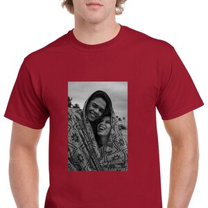 May include: A maroon t-shirt featuring a black and white photograph of two people smiling and wrapped in a patterned blanket. The photograph is centered on the shirt.