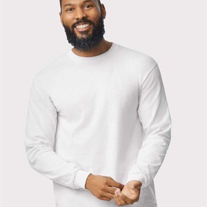 May include: A plain white long-sleeve t-shirt featuring a classic crew neckline and fitted cuffs at the wrists. The garment is constructed from a solid white fabric with a smooth texture, providing a clean and simple appearance for everyday wear.