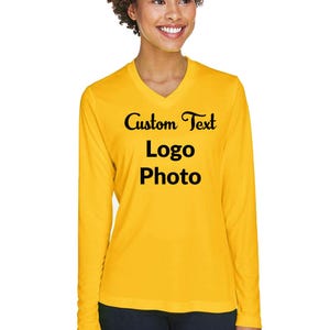 May include: A long-sleeved, yellow V-neck shirt with the words "Custom Text Logo Photo" in black script. The shirt is made of a smooth fabric and is being worn by a person.