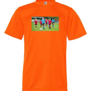 May include: Orange short-sleeved t-shirt with a graphic of children playing soccer on a green field