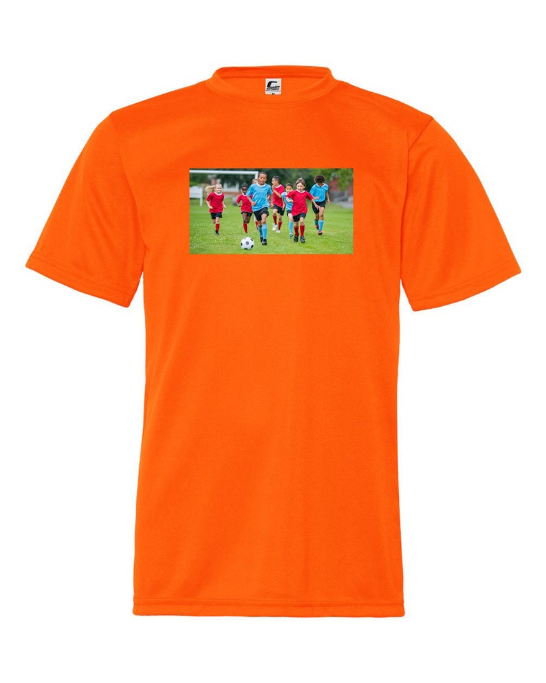 May include: Orange short-sleeved t-shirt with a graphic of children playing soccer on a green field