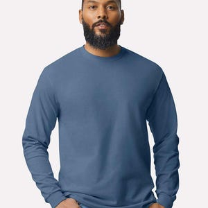 May include: A solid slate blue long-sleeve crew neck t-shirt made of a smooth fabric. The shirt features a standard fit with long sleeves that end in ribbed cuffs and a classic round neckline, providing a simple and clean appearance for daily wear.