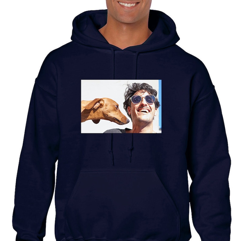 May include: A navy blue hooded sweatshirt featuring a rectangular graphic print on the chest. The print displays a photograph of a smiling person wearing sunglasses next to a brown dog looking toward the person's face, set against a white background.