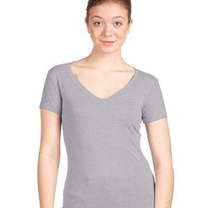 May include: A heather gray short-sleeved t-shirt featuring a deep V-neckline. The garment is constructed from a soft, lightweight fabric with a subtle marled texture, providing a fitted silhouette that sits comfortably against the torso.