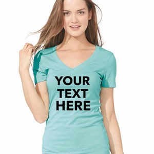 May include: A teal short-sleeved v-neck t-shirt featuring the black text YOUR TEXT HERE printed in a bold sans-serif font across the chest. The garment is paired with light pink and white horizontal striped shorts visible at the bottom hem.