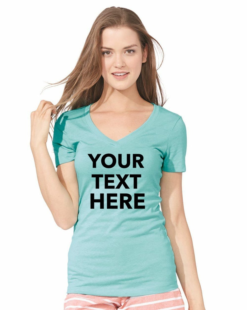 May include: A teal short-sleeved v-neck t-shirt featuring the black text YOUR TEXT HERE printed in a bold sans-serif font across the chest. The garment is paired with light pink and white horizontal striped shorts visible at the bottom hem.