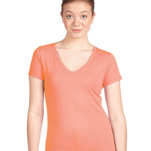 May include: A solid coral-colored short-sleeve t-shirt featuring a deep V-neckline. The garment is constructed from a smooth, lightweight fabric and has a fitted silhouette with short sleeves and a straight hemline at the waist.