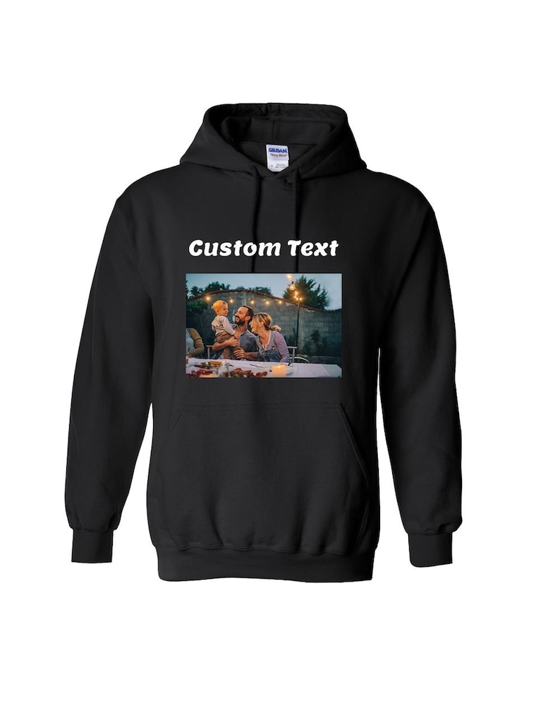 May include: A black hooded sweatshirt featuring a rectangular graphic print on the chest. The print displays a photograph of a family dining outdoors at dusk with string lights. Above the photograph, the words Custom Text are printed in white.