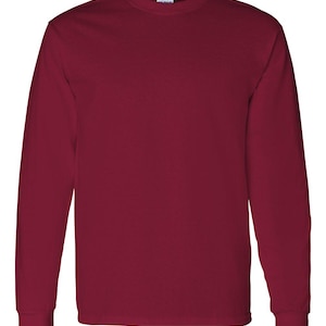 May include: A solid maroon long-sleeve crew neck t-shirt with a plain design. The garment features a standard ribbed collar and long sleeves with cuffs at the wrists. A small white brand label is visible on the inside of the neckline.