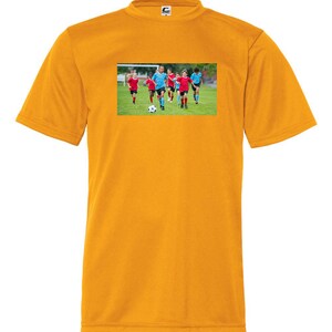 May include: A yellow t-shirt with a graphic of a group of children playing soccer on a green field