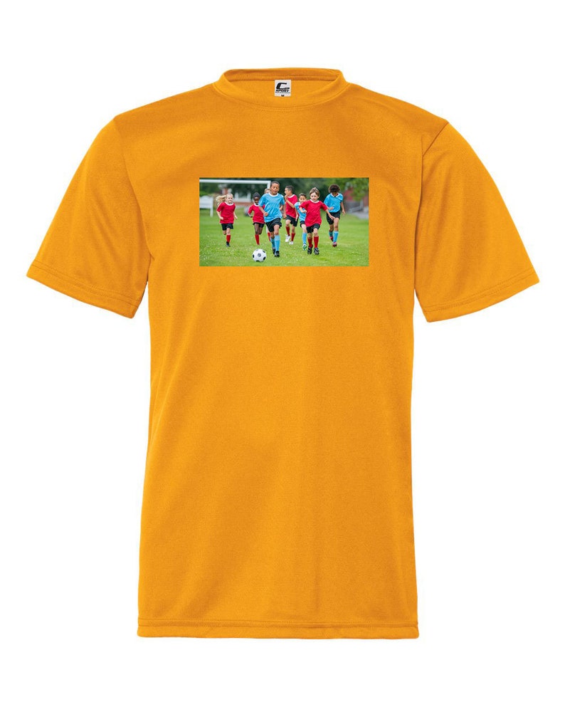May include: A yellow t-shirt with a graphic of a group of children playing soccer on a green field