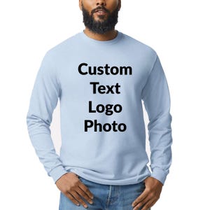 May include: A light blue long-sleeve crew neck shirt featuring the black printed text Custom Text Logo Photo centered on the chest. The garment has a standard fit with ribbed cuffs at the wrists and a simple round neckline design.
