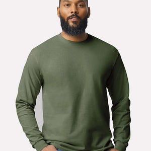 May include: A long-sleeve crew neck t-shirt in a solid olive green color. The garment features a standard fit with ribbed cuffs at the wrists and a simple, unadorned design. The fabric appears to be a smooth, opaque cotton-blend material.