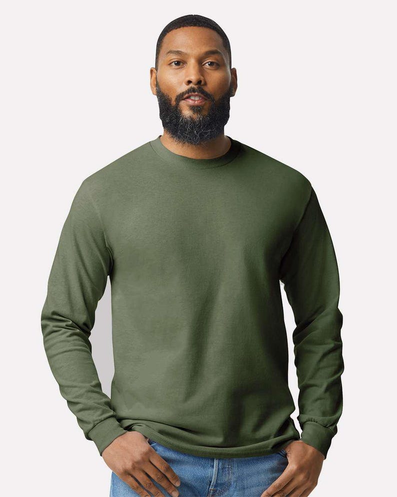 May include: A long-sleeve crew neck t-shirt in a solid olive green color. The garment features a standard fit with ribbed cuffs at the wrists and a simple, unadorned design. The fabric appears to be a smooth, opaque cotton-blend material.