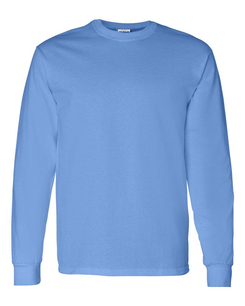 May include: A solid light blue long-sleeve t-shirt with a crew neckline and ribbed cuffs. The garment features a plain, unpatterned design with a visible brand label located at the inner back of the collar, providing a simple and clean aesthetic.