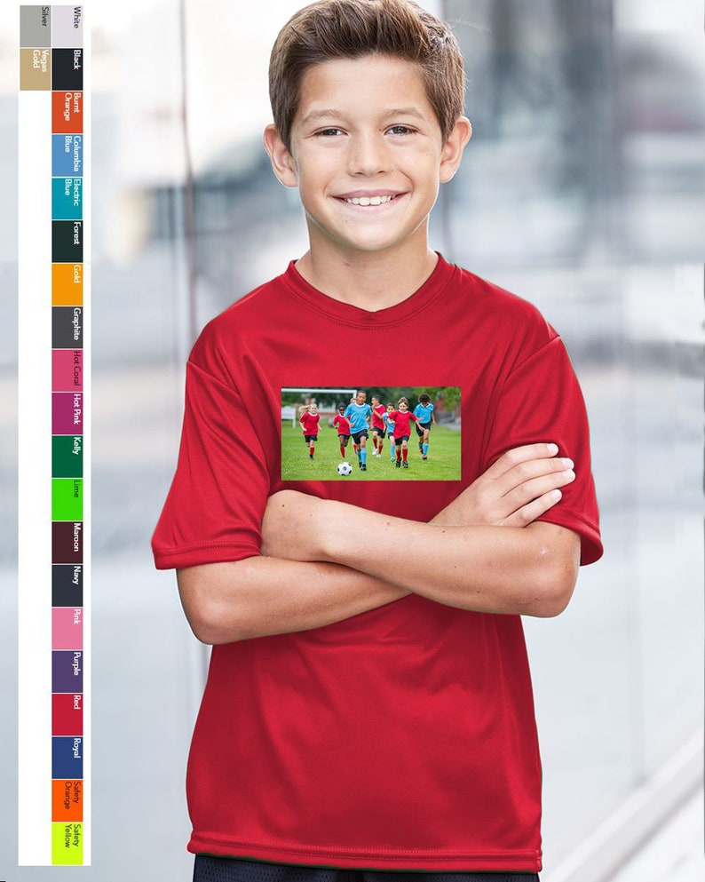 May include: A red youth-sized performance t-shirt with a graphic of a soccer team playing on a green field.