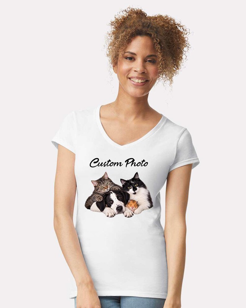 Op de afbeelding: Een wit T-shirt met V-hals voorzien van een grafische print van een cyperse kat, een zwart-witte kat, een zwart-witte hond en een kleine hamster die tegen elkaar aan liggen. De tekst Custom Photo staat in zwarte letters boven de illustratie.