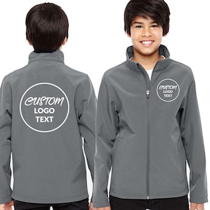May include: A gray softshell jacket with a full zipper and a stand-up collar. The jacket features a white circular logo with the text "CUSTOM LOGO TEXT" on the front and back. The jacket is shown on a young person.