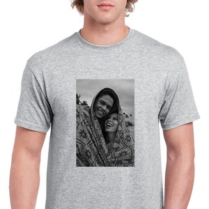May include: A gray t-shirt featuring a black and white photograph of two people smiling and wrapped in a patterned blanket. The photograph is centered on the shirt.