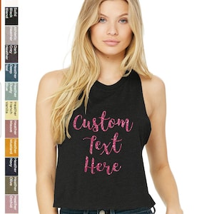 May include: A black racerback tank top with a cropped hem. The tank top has the words "Custom Text Here" printed on the front in pink glitter.