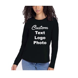 May include: A black long-sleeve shirt featuring white text printed on the chest that reads Custom Text Logo Photo. The shirt has a crew neckline and is paired with blue denim jeans. The design is centered on the front of the garment.
